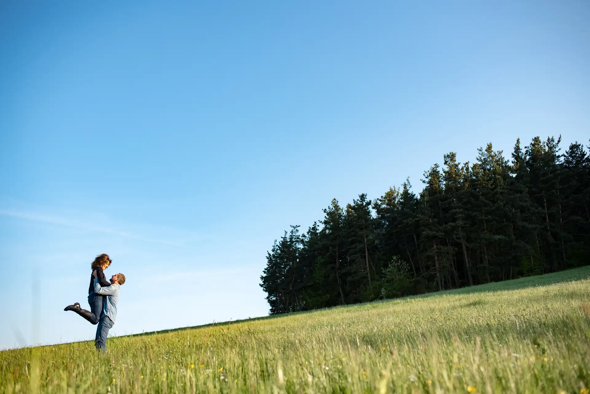 Séance photo couple fiançailles dans un champs devant la forêt - l'homme jette en l'air la femme